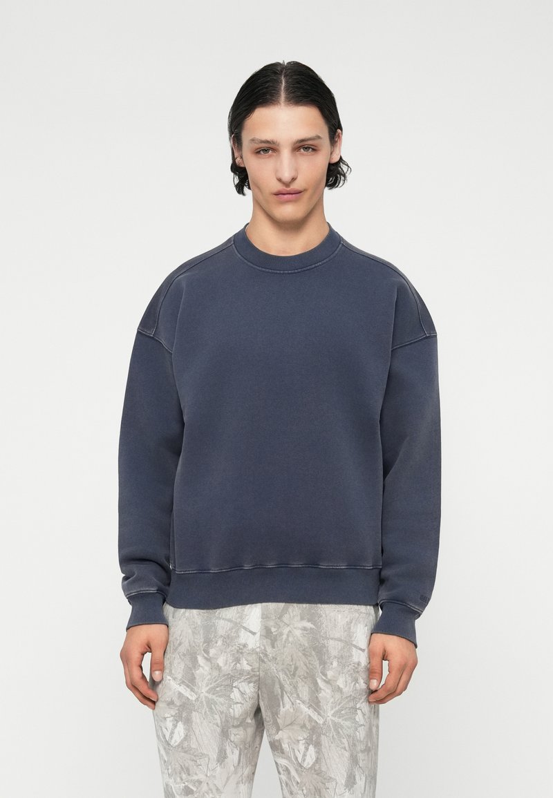 Σκούφος ναυτικού χρώματος με στρογγυλή λαιμόκοψη, χαμηλωμένους ώμους και ριμπ μανσέτες. Το ύφασμα φαίνεται μαλακό με λεία υφή.