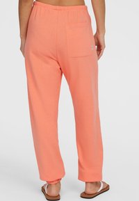 Coral joggerbroeken gemaakt van zacht materiaal, met een elastische tailleband en een enkele achterzak; taps toelopende boorden bij de enkels.