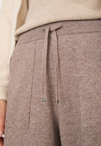Brązowe dzianinowe spodnie dresowe o miękkiej strukturze, z elastycznym paskiem i dyskretną metką marki. Model ma luźny krój i boczne kieszenie.