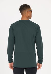 Langärmliges Sportshirt in dunklem Grün, mit einem strukturierten oberen Bereich und einem glatten unteren Bereich. Lässiger Schnitt mit Raglanärmeln.