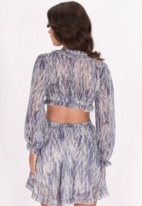 Doorzichtig tweedelig set in blauw en room met een bladpatroon, bestaande uit een cropped top met ruches en een bijpassende uitlopende rok.