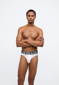 Λευκά βαμβακερά εσώρουχα με μαύρη ζώνη Calvin Klein, εφαρμοστό σχέδιο, λεία υφή και μινιμαλιστικό στυλ, εκτεθειμένα σε μοντέλο που στέκεται.