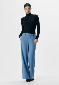 Sort turtleneck-top og lysblå vidde bukser med frontfolder, der har sidelommer og en glat stoftekstur.