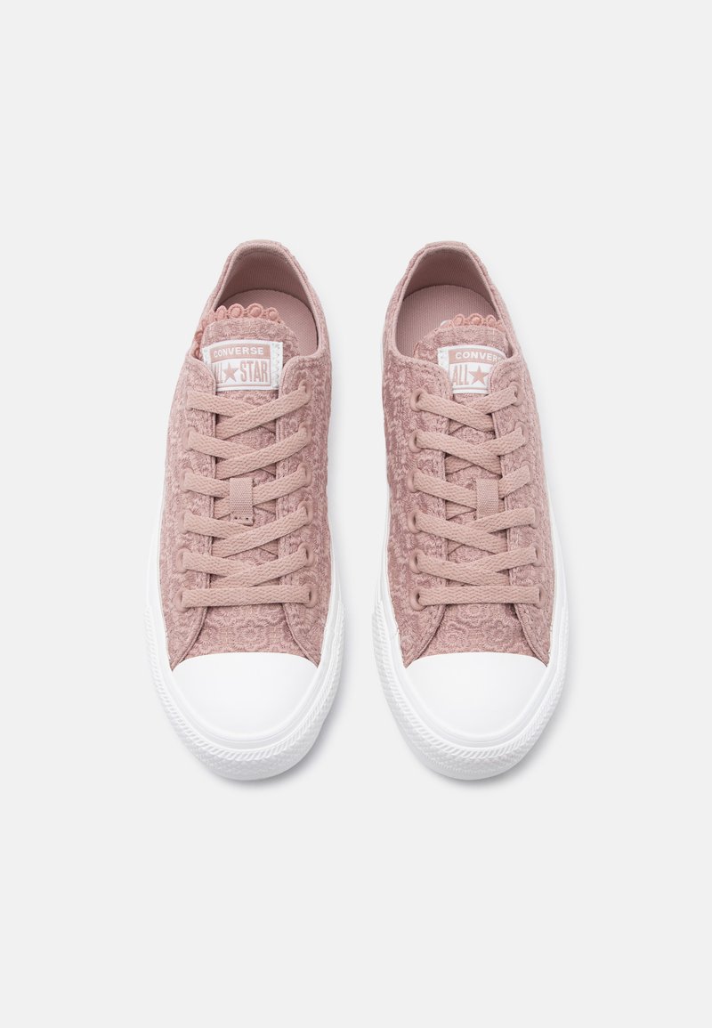Paar pinkfarbene Converse-Sneaker aus Spitze mit weißen Gummikappen an den Zehen und Sohlen, von oben auf einem schlichten Hintergrund betrachtet.