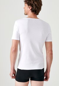 White short-sleeve T-shirt made of cotton, featuring a crew neck and a smooth texture, worn with black briefs, showing the back view.