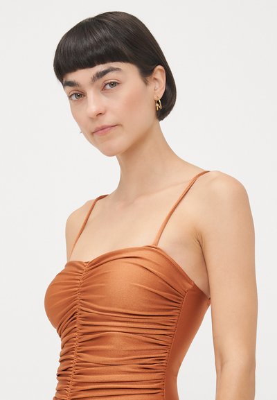 Brown ruched dress with thin straps, made from a sleek, shiny fabric. Features a fitted design that accentuates the silhouette.