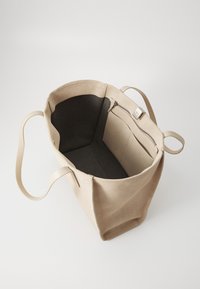 Lærred tote taske i lys beige med en blød tekstur, der har en sort indvendig, en lynlås lomme og lange flade stropper.
