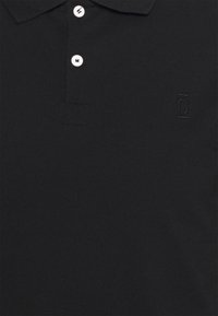 Polo noir en tissu à tissage texturé. Doté d'un col classique, d'une patte de boutonnage à trois boutons et de détails de logo en relief.