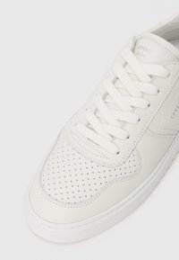 White leather sneaker with perforated toe, white laces, and subtle branding "Copenhagen Studios" on the tongue and side panel.