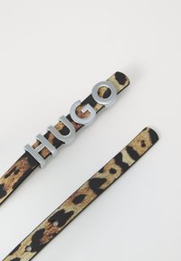 Čierny vegánsky kožený opasok s leopardím vzorom, so zaoblenou striebornou kovovou prackou, na ktorej je v veľkých písmenách napísané "HUGO".