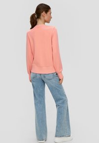 Lichtroze sweatshirt met een ronde hals en ribgebreide manchetten, gecombineerd met high-waisted lichtblauwe wijde jeans en witte platform sneakers.