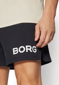 Juodi sportiniai šortai su baltu „BORG“ logotipu, pagaminti iš lengvos medžiagos, su šoniniu plyšiu ir elastingu juosmeniu.