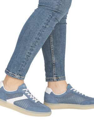 Person trägt blaue Mesh-Sneaker mit weißen Akzenten und hellbeigen Sohlen, kombiniert mit hochgekrempelten blauen Denim-Jeans.