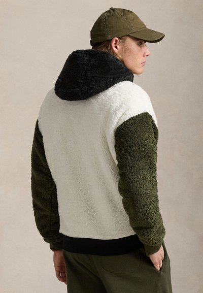 Pull en polaire dans les teintes crème, vert olive et noir. Doté d'une capuche, d'un tissu texturé et de poignets côtelés. Coupe décontractée avec un design sportif.