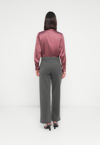 Camicia in satin bordeaux a maniche lunghe abbinata a pantaloni grigi a gamba larga e tacchi neri con una tracolla a fantasia, vista da dietro.