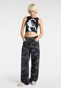 Cropped black tank top with a white scorpion graphic, paired with high-waisted camo pants in shades of gray, featuring side pockets and relaxed fit.