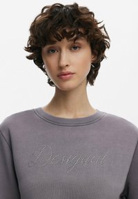 Hall hallidega hall dressipluus, millel on ribidega ümar kaelus ja esik�üljel on "Desigual" tekst, kaunistatud vääriskividest. Pehme materjal ja mugav lõige.