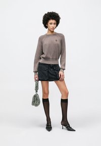 Pruun soonikuga kampsun ümarseljaga, must teksaseelik taskutega, läbikumavad mustad põlvikud, mustad teravate ninadega kontsakingad, roheline kott.