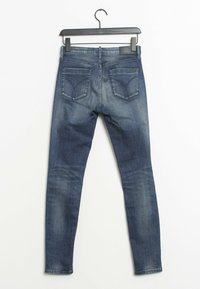Slim-fit denimjeans i mörkblått med ljus blekning. Har en medelhög midja och två bakfickor, hängande från en svart galge.