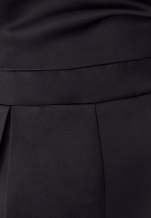 Tejido negro con una textura suave y un ligero brillo. Diseño plisado en la parte inferior con una cinturilla limpia. Sin hardware o patrones visibles.