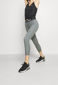 Leggings sportivi grigi con vita nera e testo "NIKE PRO", abbinati a una canotta nera e scarpe da ginnastica nere.