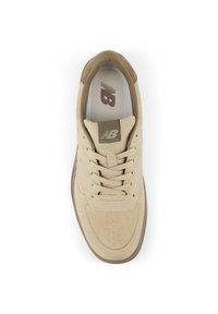 Αθλητικό παπούτσι από μπεζ σουέντ με στρογγυλή μύτη, διάτρητες λεπτομέρειες στο μπροστινό μέρος και κορδόνια στο ίδιο χρώμα. Διαθέτει υφασμένο λογότυπο σε ταμπά χρώμα στη γλώσσα.