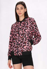Giacca bomber con stampa leopardata rosa e nera, con chiusura a zip, polsini e orlo a costine. Indossata sopra pantaloni corti neri, presenta una vestibilità rilassata.