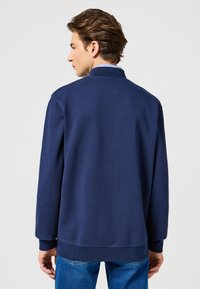 Mörkblå sweatshirt med hög krage, ribbstickade muddar och fåll. Mjukt bomullsmaterial med slät finish. Enkel design utan synliga mönster.