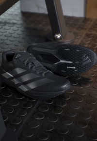 Ζευγάρι μαύρα παπούτσια τρεξίματος Adidas σε υφή από καουτσούκ στο γυμναστήριο κοντά σε εξοπλισμό άσκησης.
