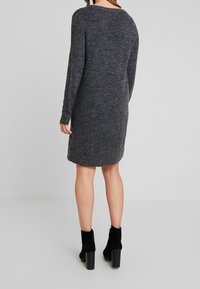Robe en maille gris foncé à manches longues avec une coupe décontractée. Elle présente un col rond et un ourlet se terminant juste au-dessus du genou, accompagnée de bottines noires.