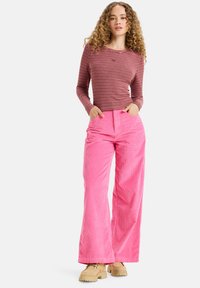 Top a maniche lunghe a righe marrone scuro abbinato a pantaloni a gamba larga in corduroy rosa. I pantaloni presentano una costina verticale; il modello indossa scarpe chunky beige.
