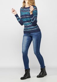 Navyblaue und türkis gestreifte Pullover mit strukturierter Stoffqualität, gerippten Bündchen, kombiniert mit enganliegenden blauen Jeans und schwarzen Schnürstiefeln im Combat-Stil.