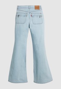 Light blue denim jeans with wide legs, back pockets with zipper details, a brown leather brand patch, and a small red tag.