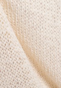 Cremfarbener, gestrickter Stoff mit lockerer Struktur, der eine weiche Textur und einen subtilen Glanz zeigt. Das Muster besteht aus verflechteten Strängen.