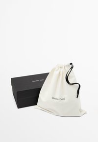 Sac en coton à cordon blanc avec le logo "Massimo Dutti", à côté d'une boîte rectangulaire noire avec une finition mate. Design simple et fonctionnel.