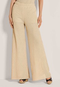 Beige gebreide broek met wijde pijpen en een gestructureerde stof, met een hoge taille en een losse pasvorm, gecombineerd met zwarte sandalen met plateauzool.