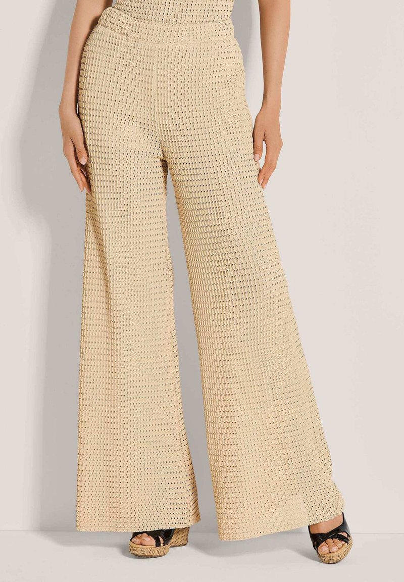 Beige gebreide broek met wijde pijpen en een gestructureerde stof, met een hoge taille en een losse pasvorm, gecombineerd met zwarte sandalen met plateauzool.