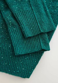 Tiefgrüne gestrickte Pulloverbündchen mit gerippten Säumen und kleinen glänzenden Pailletten, die über den Stoff verteilt sind.