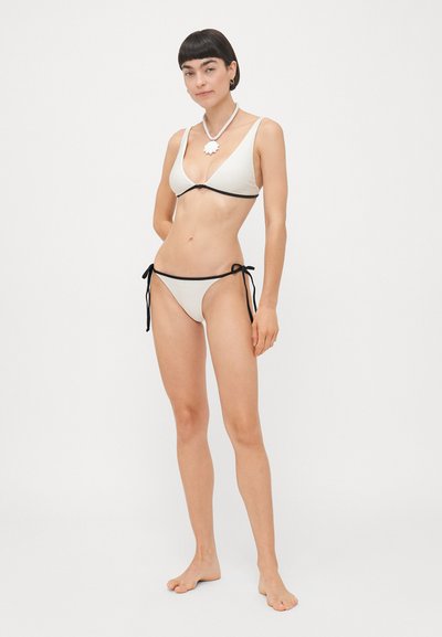 Divdaļīgs bikini gaiši bežā audumā ar melnām apmalēm. Augšdaļa ir trīsstūra formā ar plānām siksnām, bet apakšdaļai ir saitīšu aizdare.
