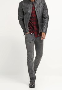 Grå læderjakke med quiltede skulderdetaljer, lag-på-lag over en rød og sortternet flannelskjorte, kombineret med grå jeans og sorte støvler.