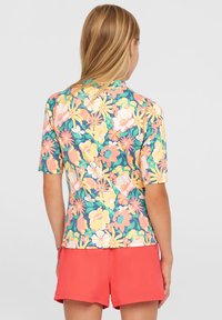 Blommig kortärmad topp med ett färgglatt mönster av rosa, gult och grönt på en marinblå bakgrund, kombinerad med korallfärgade shorts.
