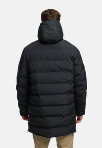 Mustassa untuvatakissa on huppu, tikatut osiot, sileä pinta ja midimittainen leikkaus. Vetoketjulliset sivutaskut näkyvissä.