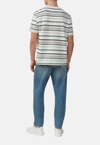 Korte mouwen gestreepte t-shirt in wit, groen en zwart, gecombineerd met lose blauwe denim jeans en witte sneakers, gezien van achteren.