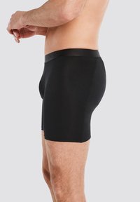 Schwarze Boxershorts aus dehnbarem Stoff, mit einem glatten Bund und Logo. Das Design schmiegt sich an den Körper an und verfügt über minimale Nähte.