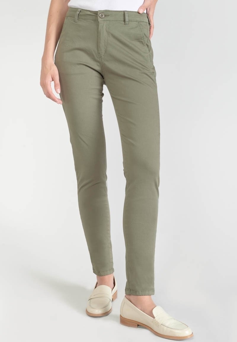 Pantalon vert olive ajusté porté avec des mocassins blancs et un haut blanc, visible de la taille aux pieds sur un fond uni.