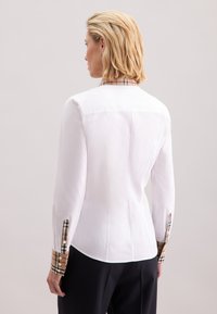 Weißes Hemd mit langen Ärmeln und Knöpfen, mit karierten Akzenten an Manschetten und Kragen. Glatter Stoff, taillierter Schnitt und dezente Details auf der Rückseite.