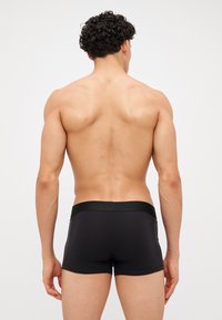 Boxer briefs pretos com uma textura suave, cintura elástica e um design ajustado, exibindo um estilo limpo e minimalista na parte de trás.