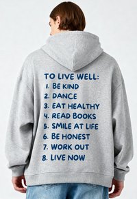 Felpa grigia con cappuccio ampio e vestibilità rilassata. Sul retro presenta un testo blu con un elenco di consigli per il benessere in un formato organizzato.