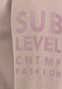 Light pink sweatshirt featuring large, embossed text in a darker shade. Soft fabric texture with a relaxed fit, no visible hardware or patterns.