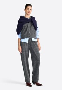 Un gilet court à carreaux gris sobre une chemise boutonnée bleu clair, associé à un pantalon large à carreaux gris et des bottines à talons foncées.